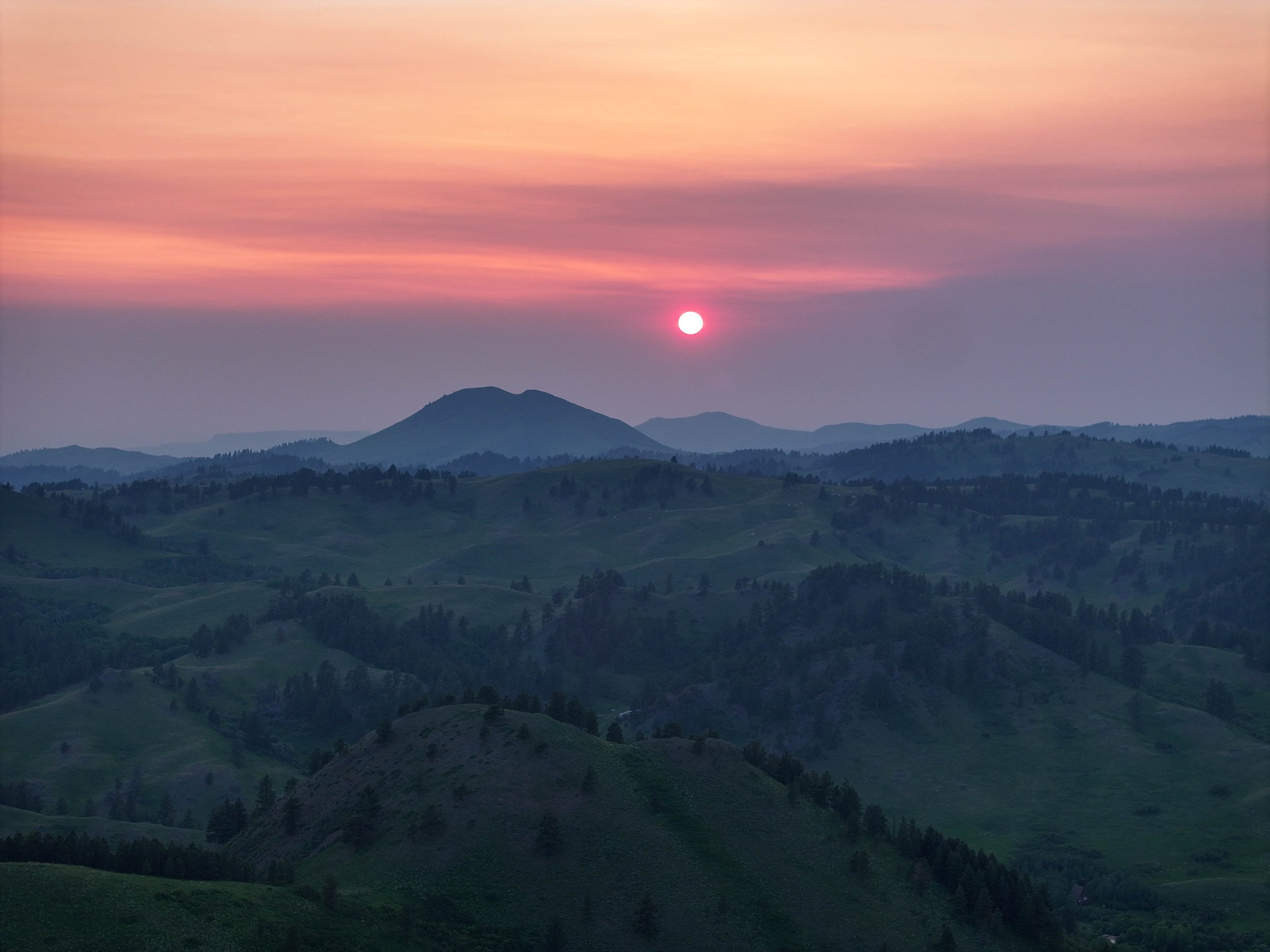 Sunset over rolling green hills and distant mountains