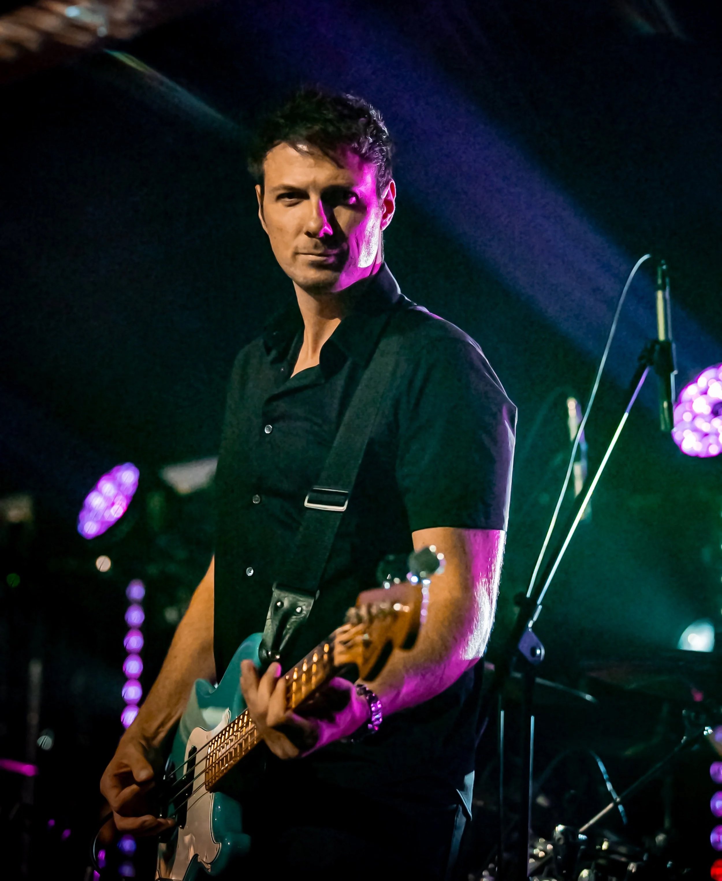 Musician playing electric guitar on stage with purple and blue lighting.