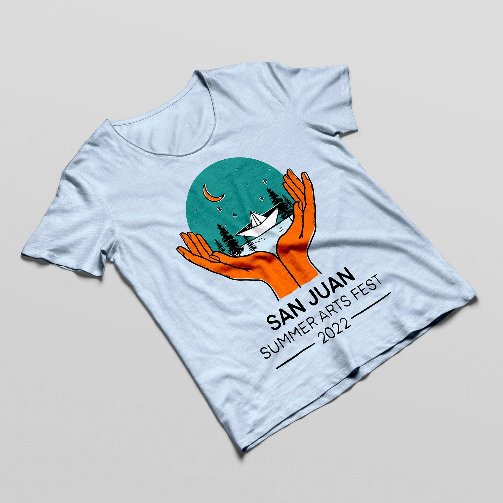 Light blue T-shirt with a graphic of orange hands holding a landscape scene with trees, stars, a crescent moon, and a paper boat, and text that reads "San Juan Summer Arts Fest 2022".