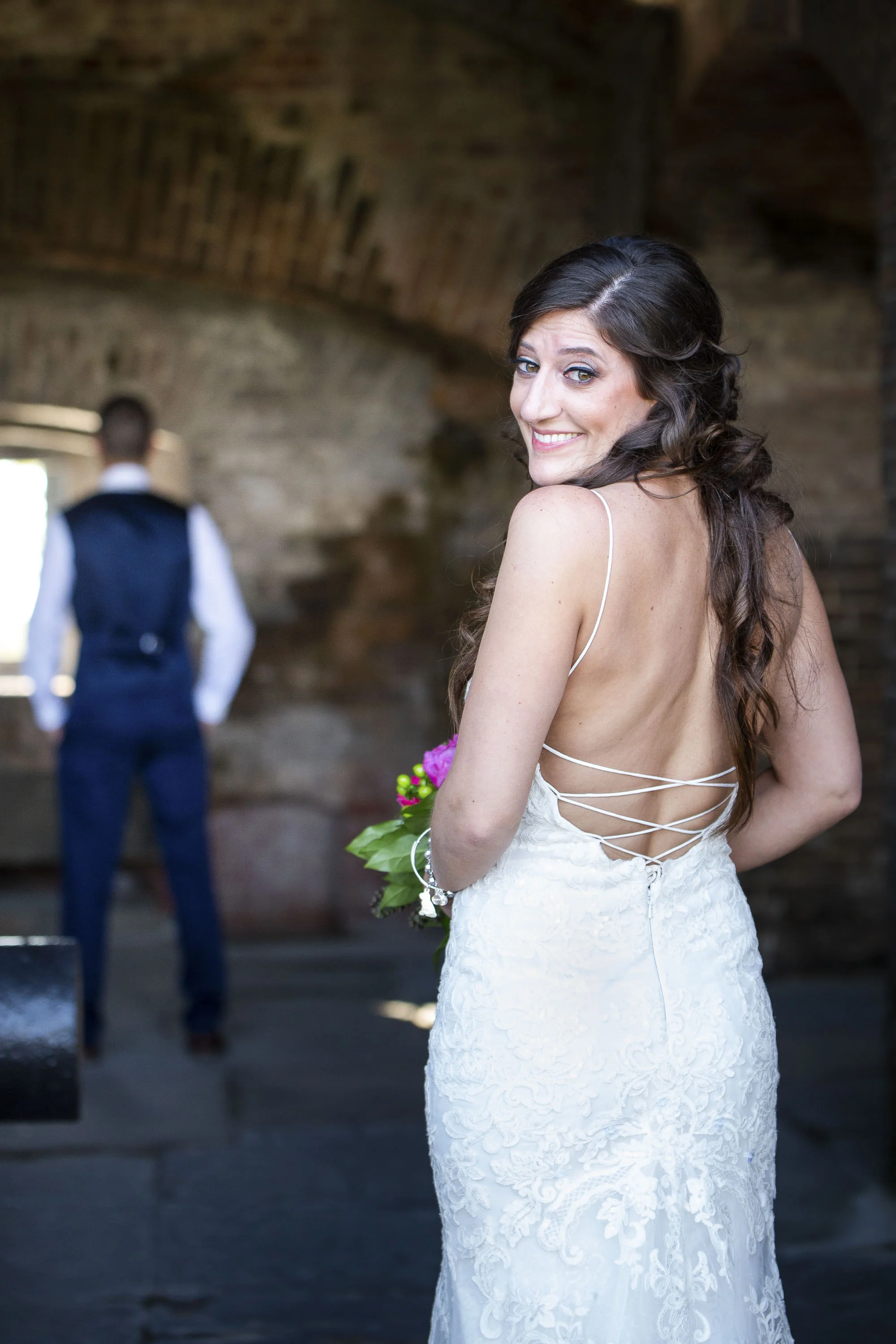 Bride peeks at camera before First Look with groom in background