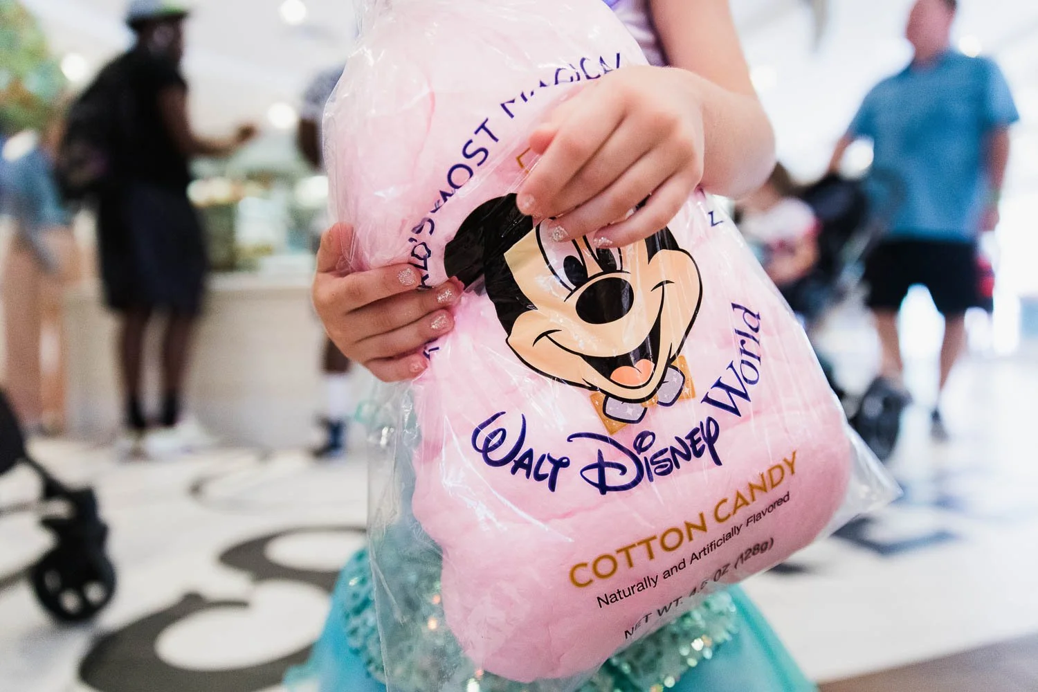 Little girl holds bag of pink cotton candy at Magic Kingdom Confectionary. 