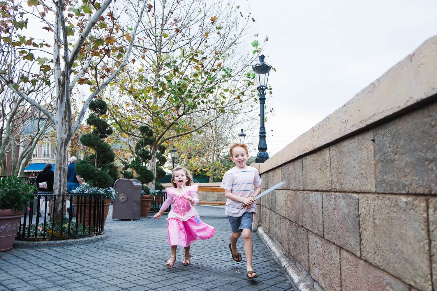 Toddler dressed like Princess Aurora and her brother run through France Pavilion at Epcot.