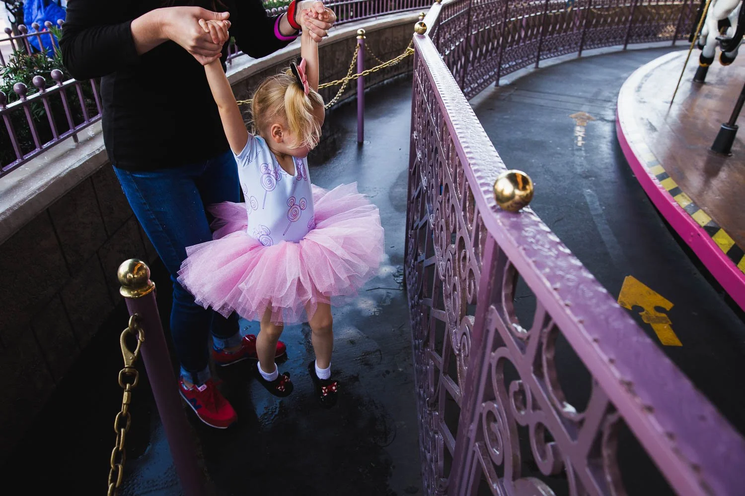 Mom lifts girl in pink tutu over a rain puddle in Fantasyland queue.