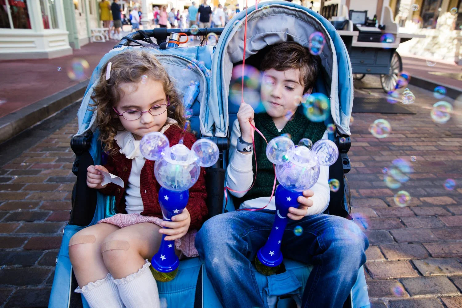 Kids in a stroller at the Magic Kingdom play with bubbles.