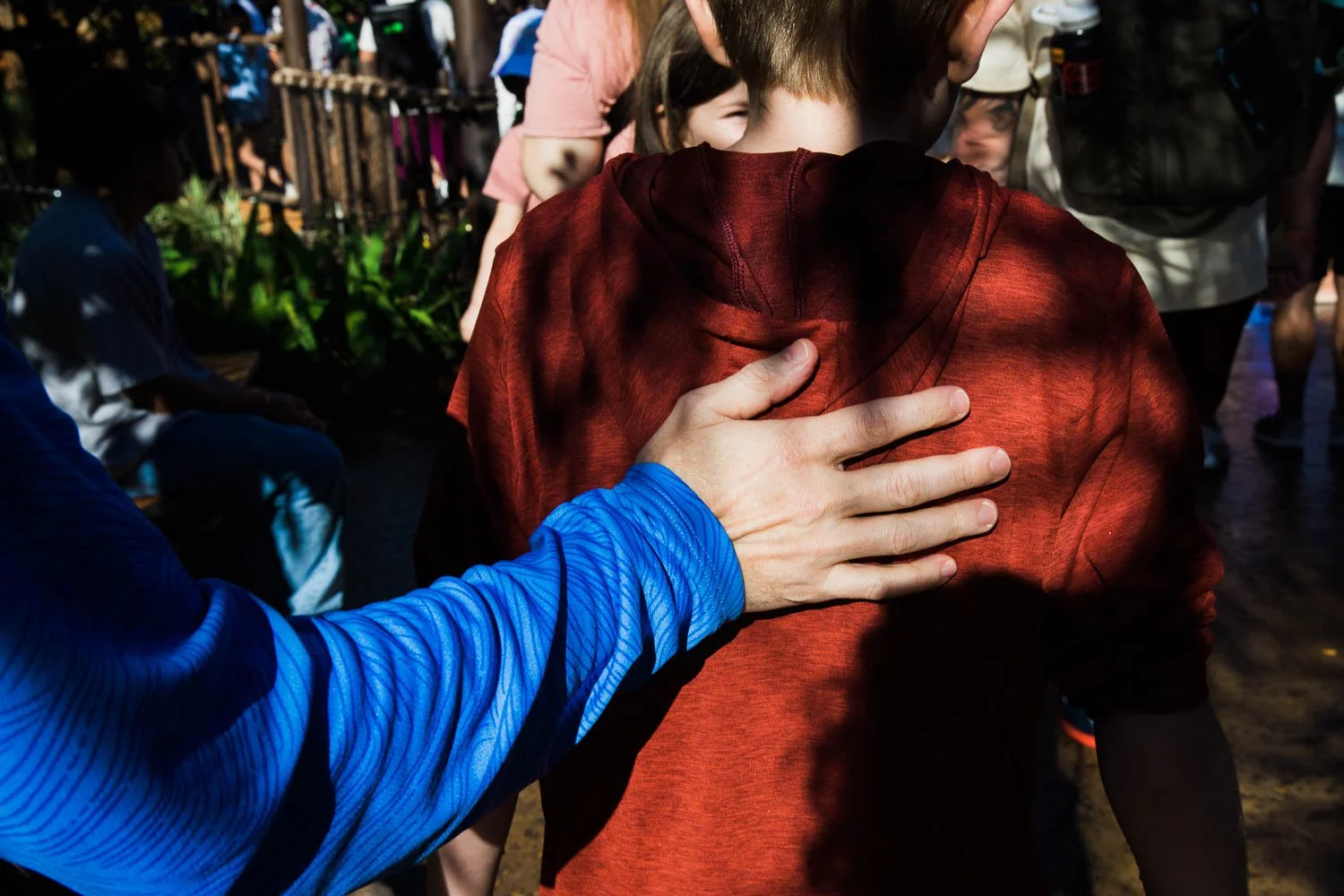 Father's hand on the back of a young boy, leading him through a crowd at Epcot.