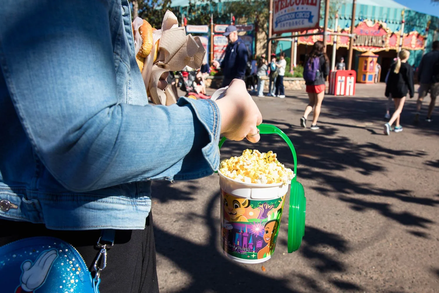 Mom carries disney popcorn bucket to her family at the magic Kingdom.