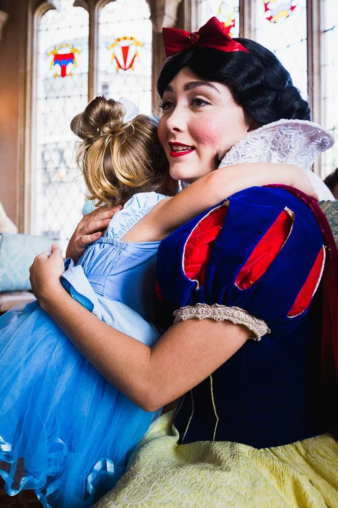Toddler dresses like Cinderella hugs Snow White at Magic Kingdom.