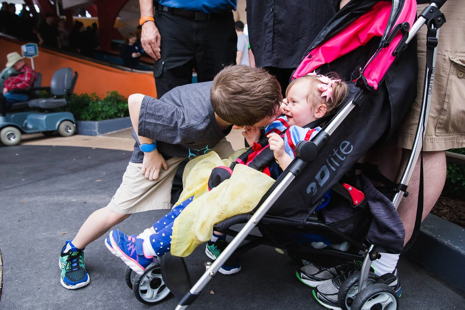 Brother leans in to give his little sister a kiss in her stroller.