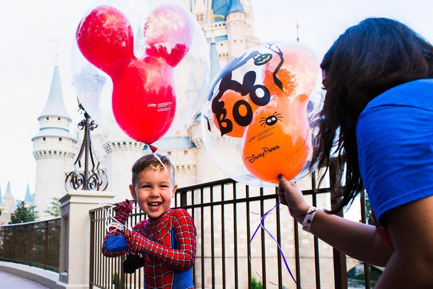 Little boy dressed as Spider-Man plays with a Mickey balloon in front of Cinderella Castle.