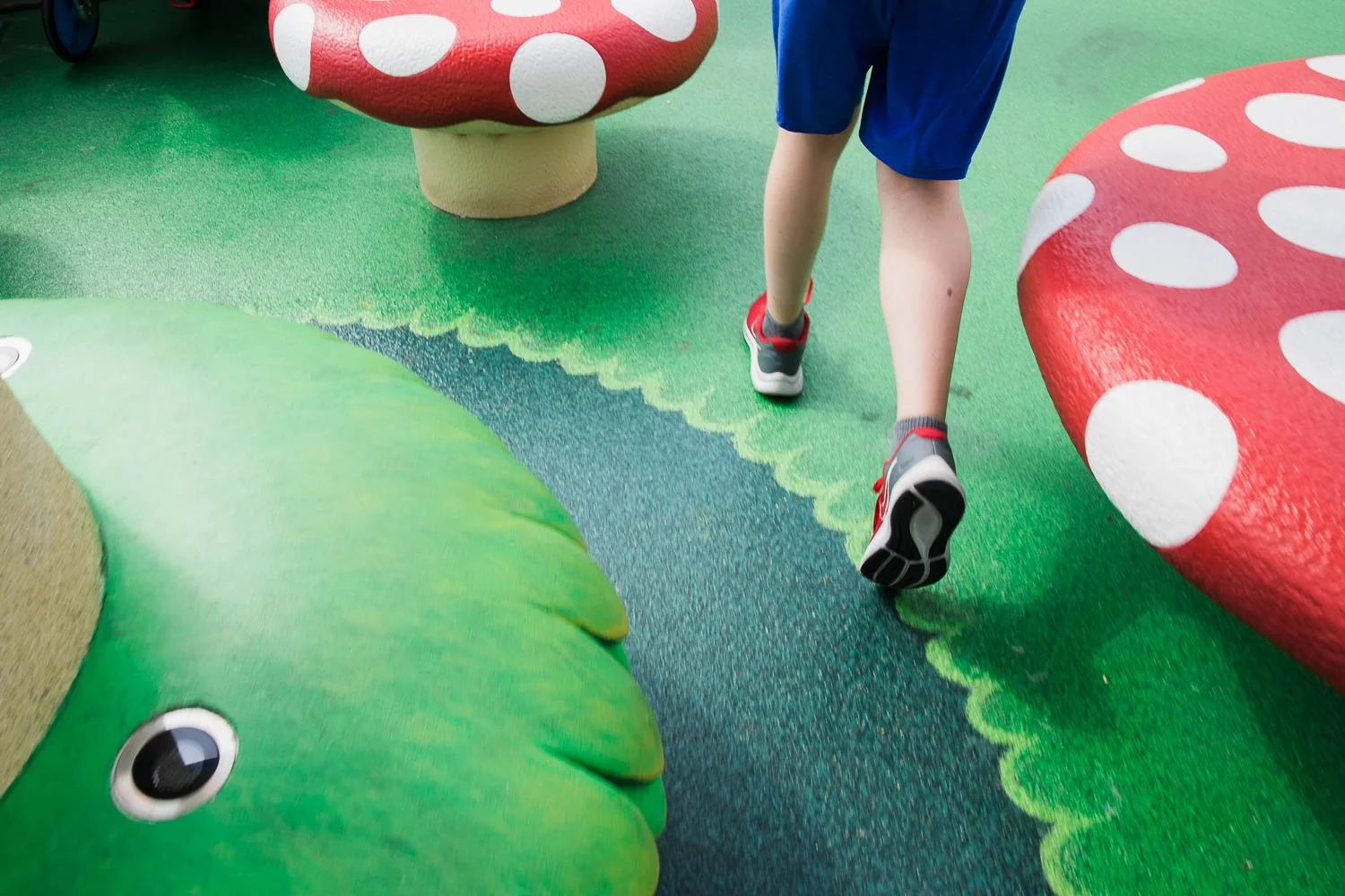 Boy in red sneakers runs past red toadstools in Super Nintendo World.