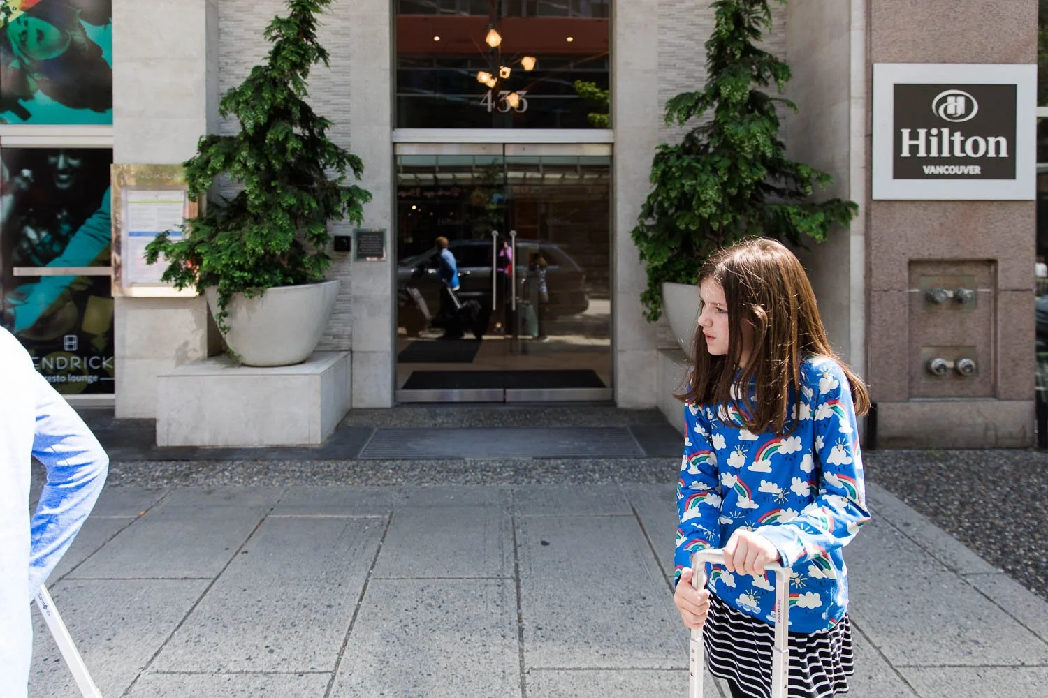Kids stand in front of the Hilton Downtown Vancouver with their luggage.