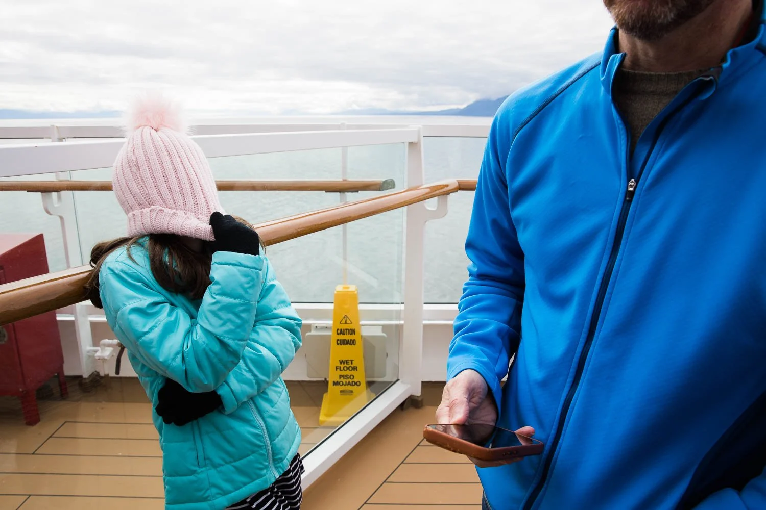 Kid covers her face entirely with a beanie while she waits in boredom to meet Mickey Mouse on an Alaska Cruise.