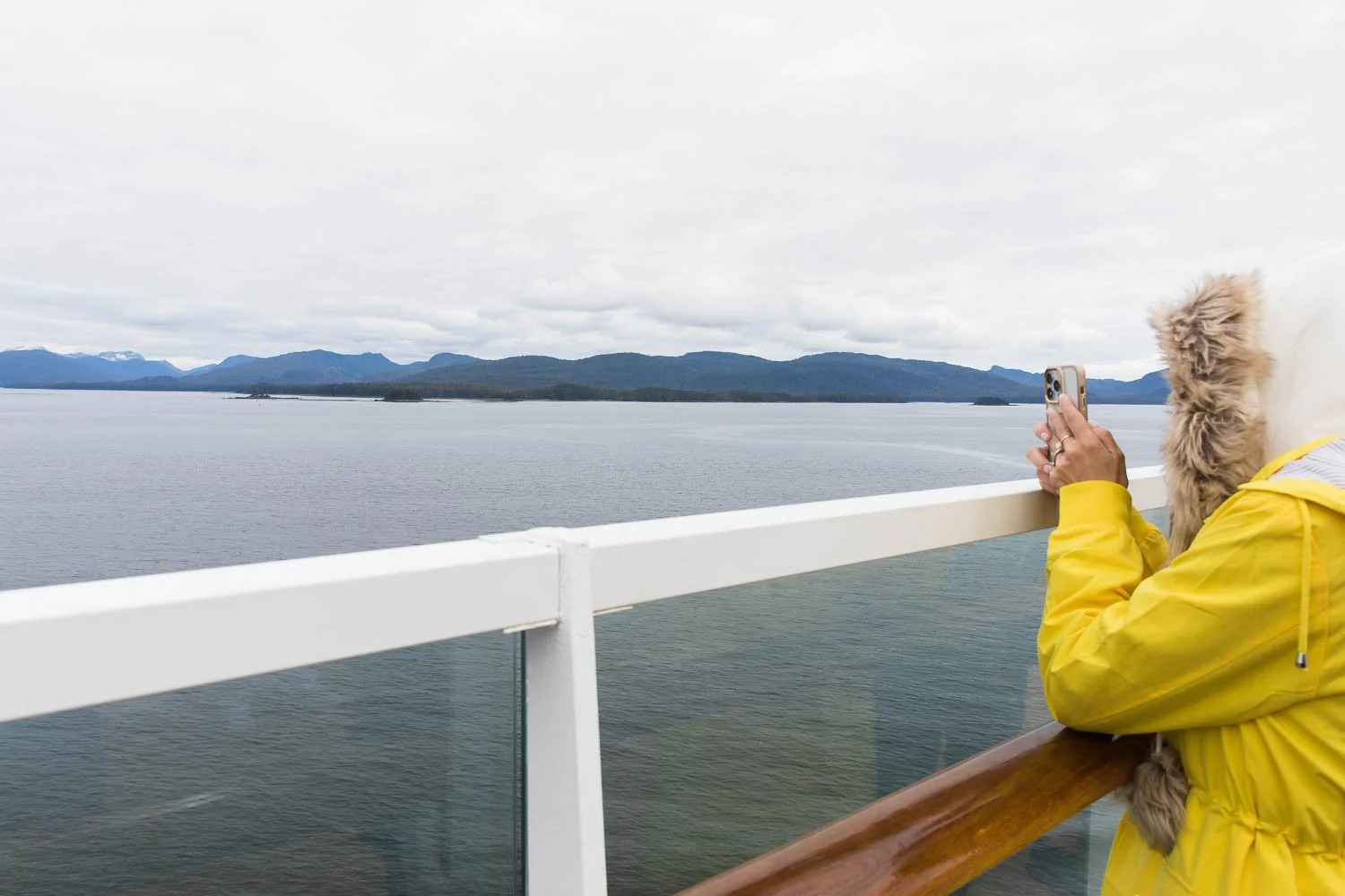 Woman dressed in rain gear takes a photo of Alaska from deck 10 of the Disney Wonder.