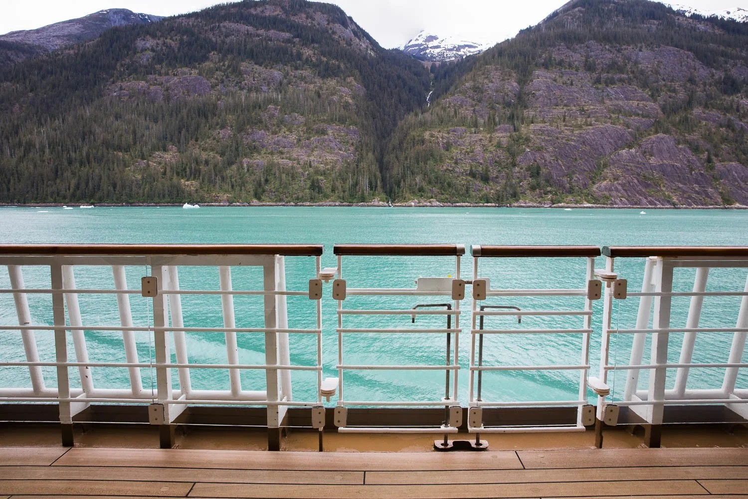 Snowcapped mountain peaks and teal blue water in the fjords of Alaska.