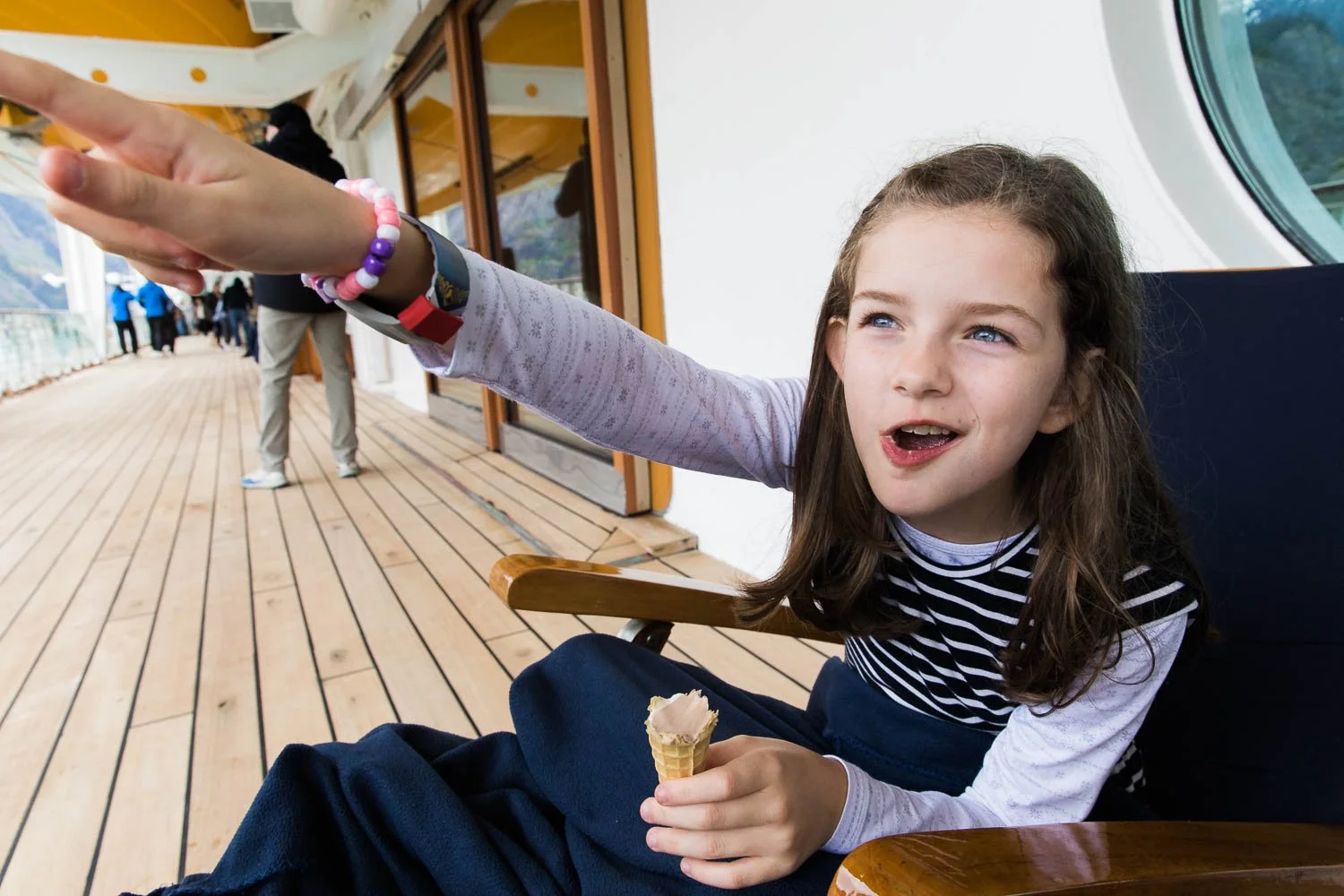 Young girl points out wildlife in Alaska while eating an ice cream cone on deck four of the Disney Wonder.