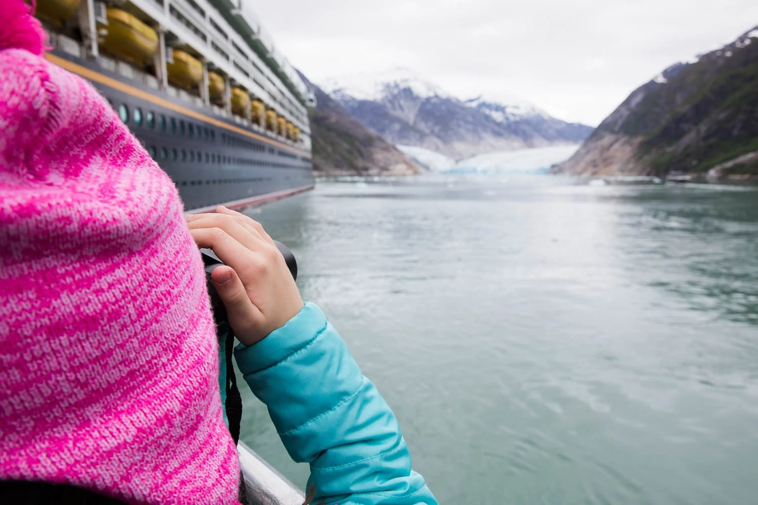 Girl looks at Disney Wonder and Alaskan glacier through binoculars.