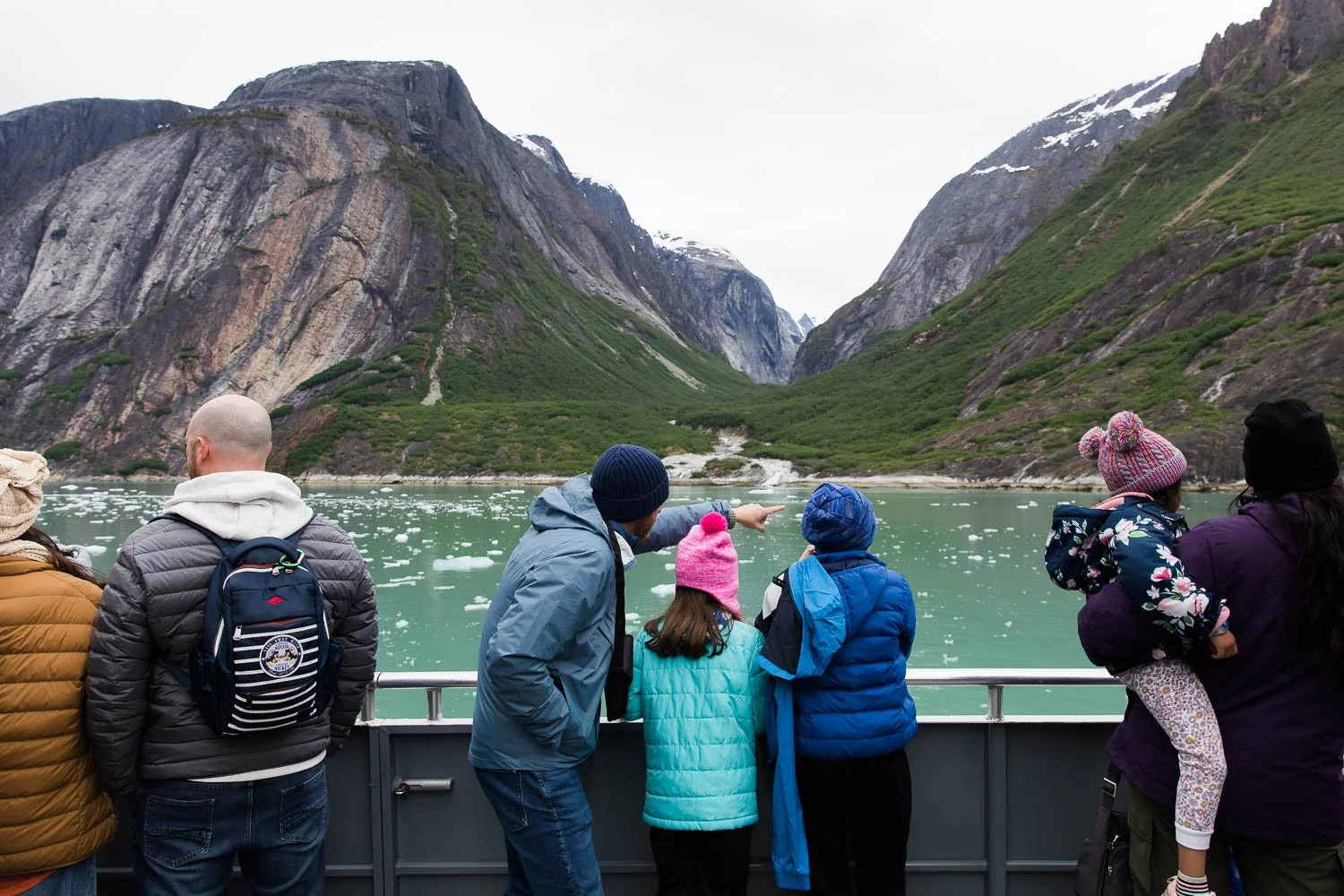 Family looks at alaskan wilderness from boat excursion.