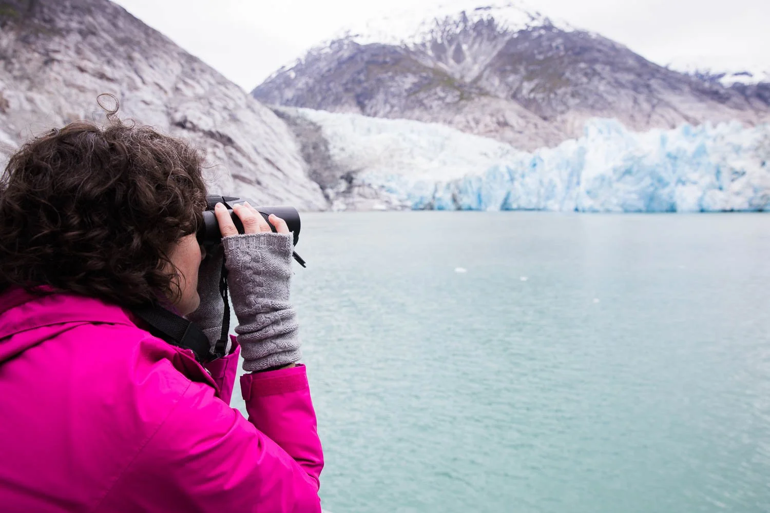 Woman looks through binoculars at Dawes Glacier.