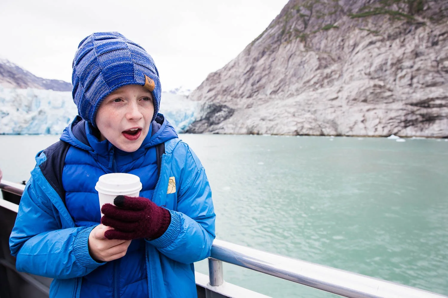 Boy drinks hot chocolate on a boat in Alaska.