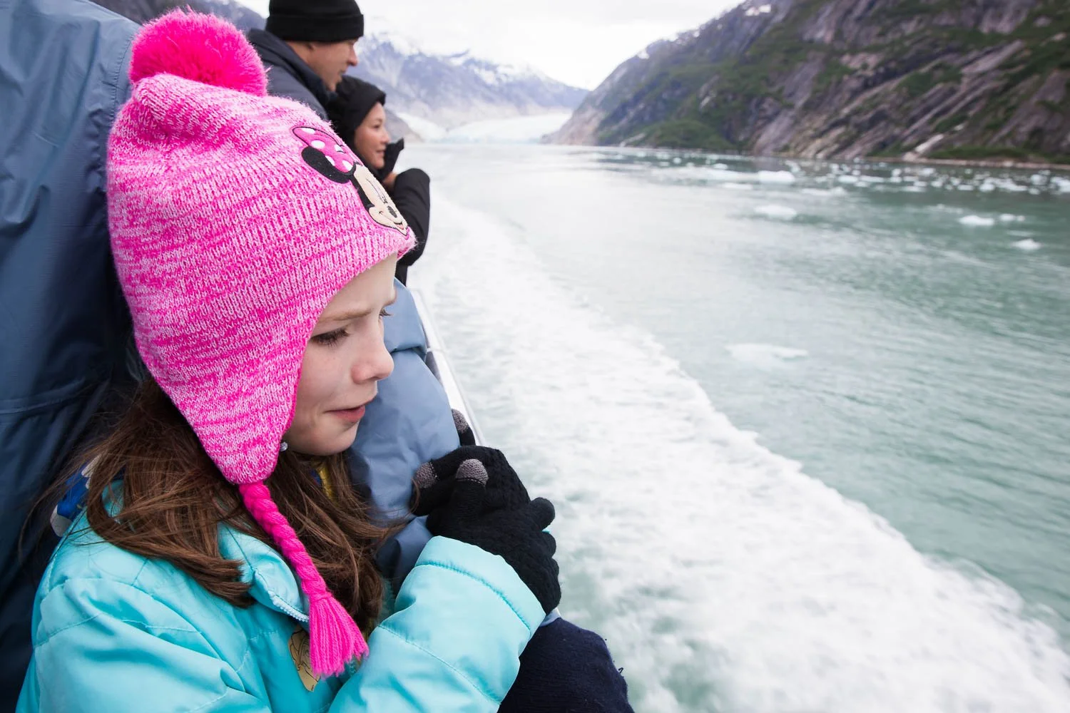 Girl holds her father's arm and looks out Alaskan fjord.