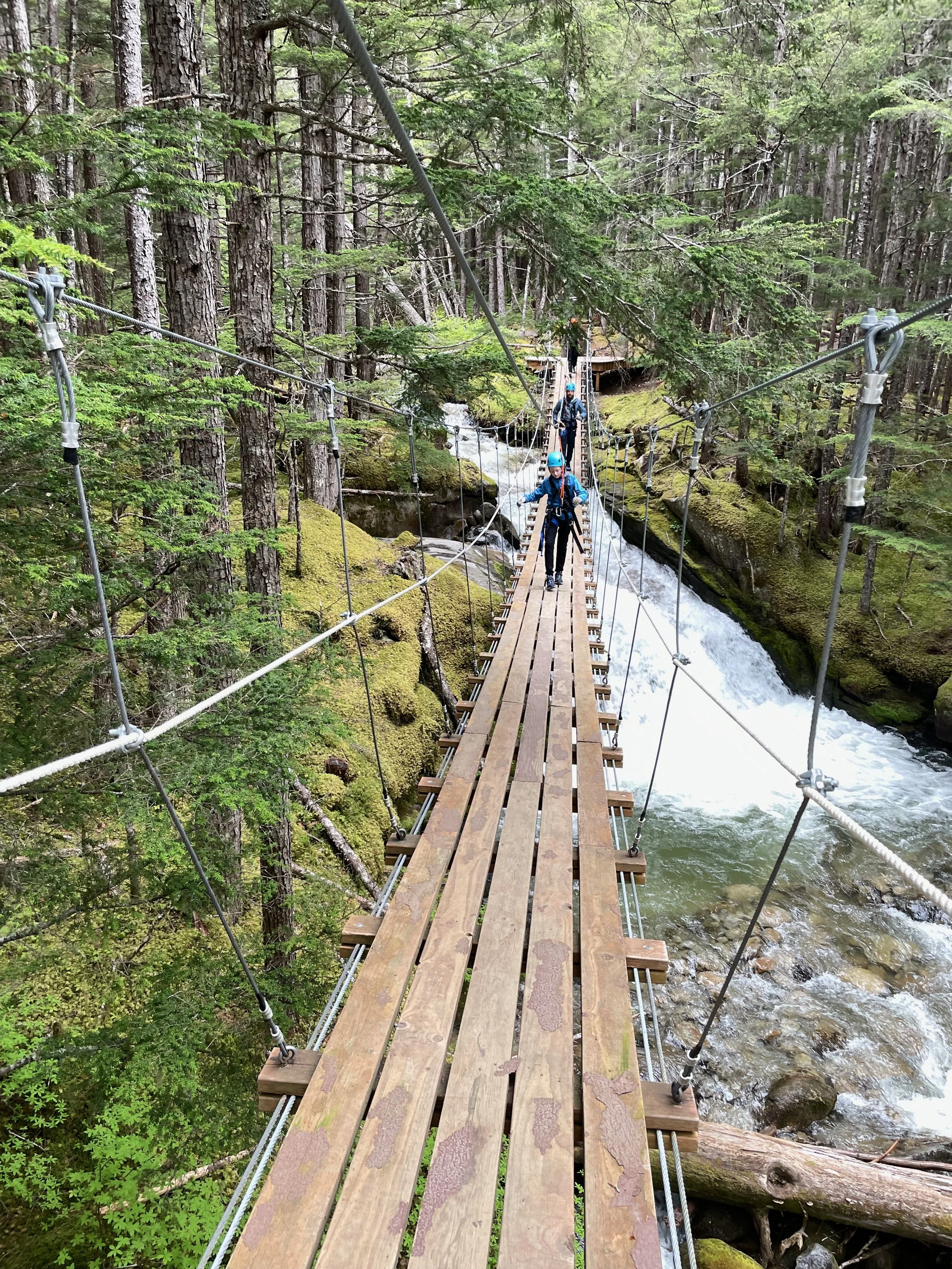 Family walks across a suspension bridge over a waterfall in Alaska.