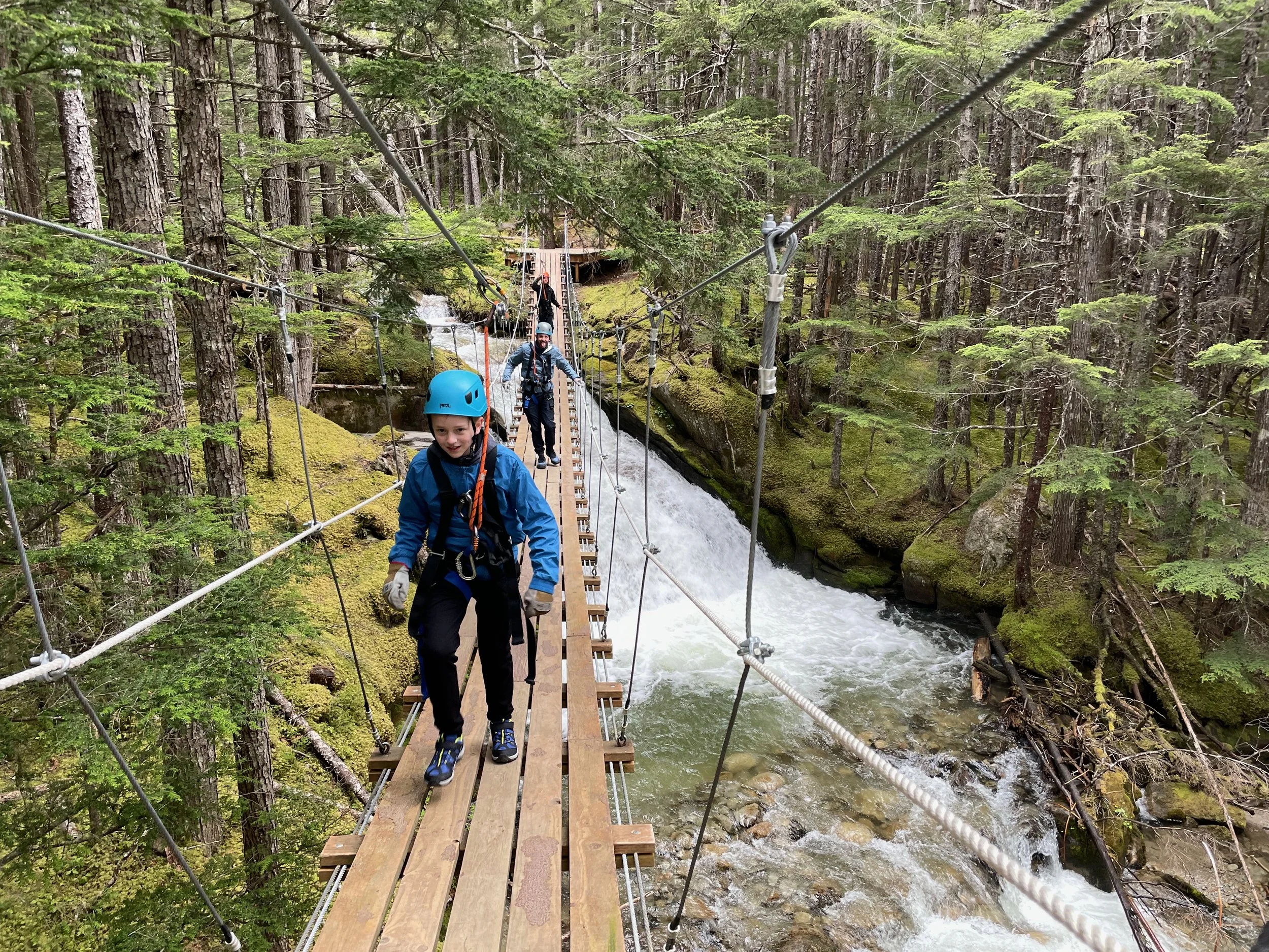 Father and son cross a suspension bridge over waterfalls in Alaska.