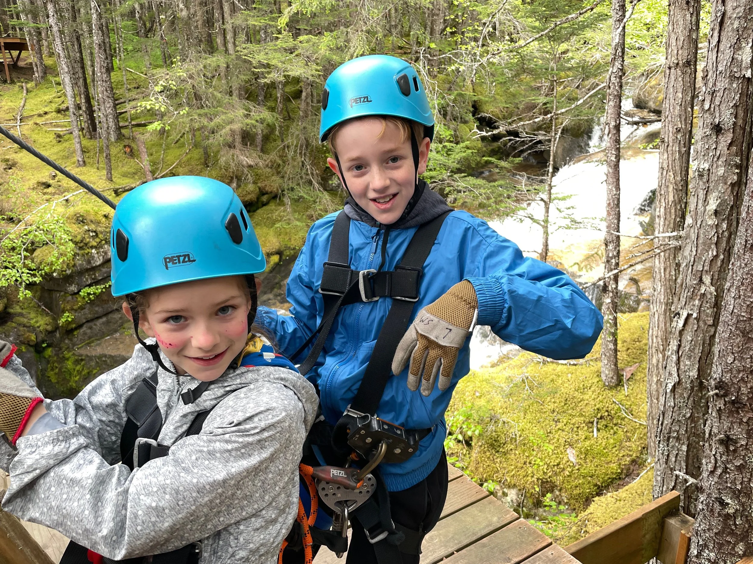 Siblings hang out over a waterfall on their zip line tour of Skagway, Alaska.