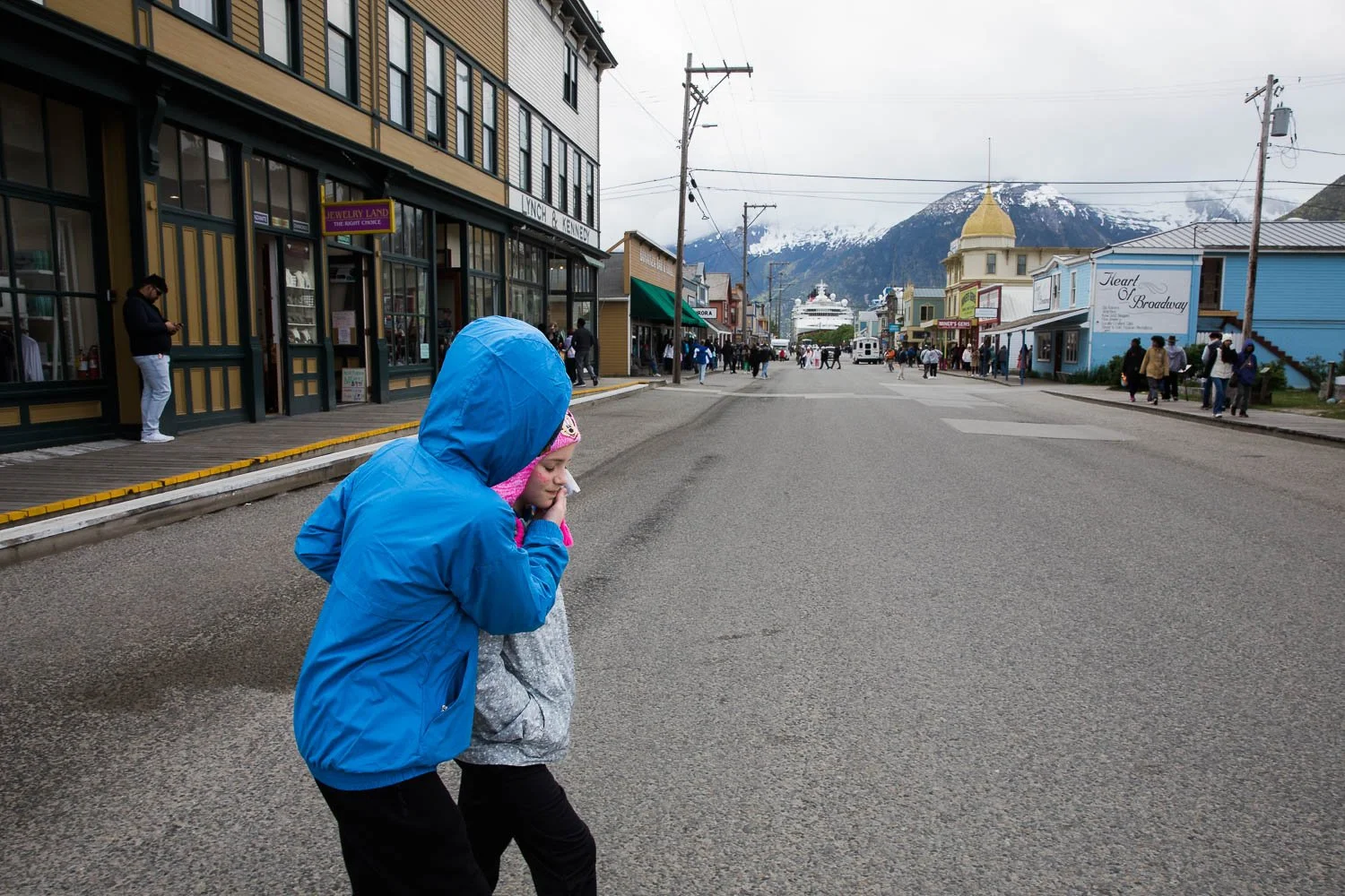 Siblings cross the street in Skagway, Alaska, with the Disney Wonder in the background.