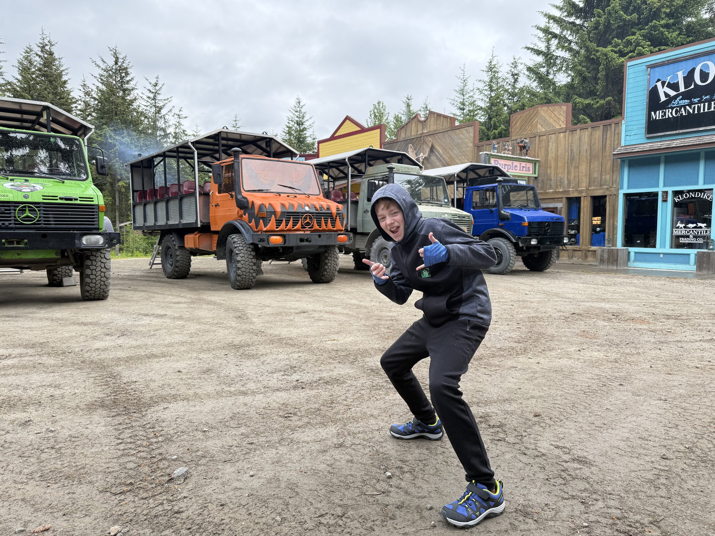 Tween boy poses in front of four wheel vehicles in Grizzly Falls, Alaska.