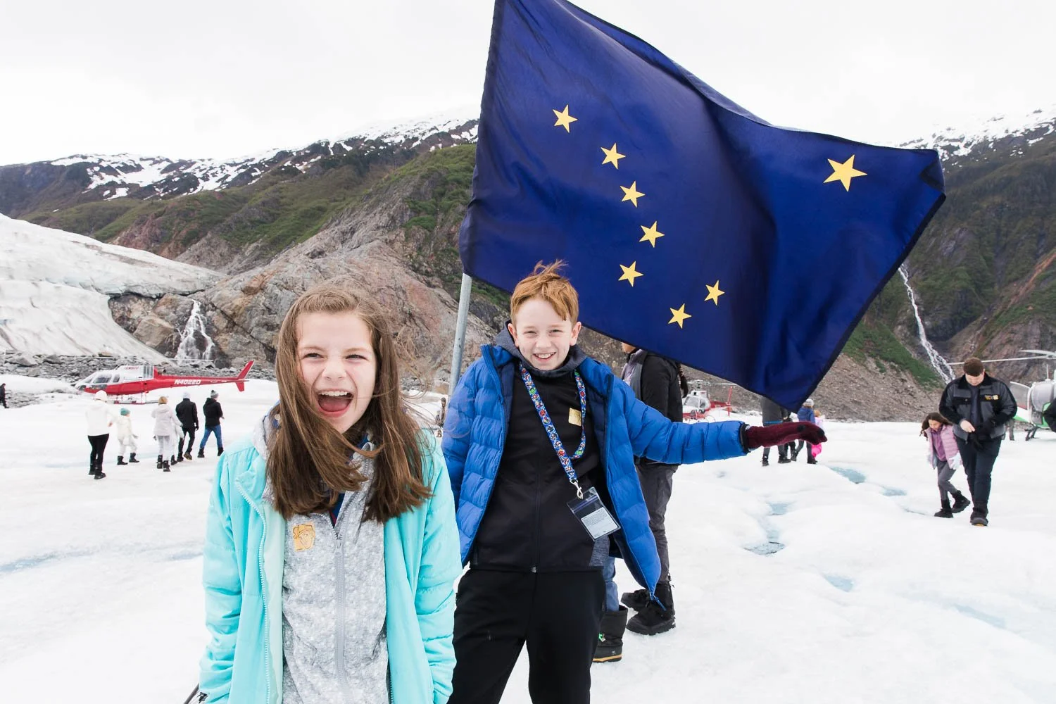 Kids stand with an Alaskan flag on the surface of Mendenhall Glacier.