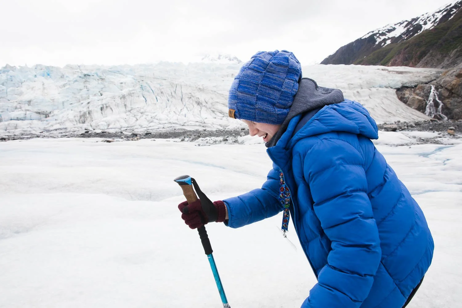 Boy uses walking stick to walk up glacier in Alaska.