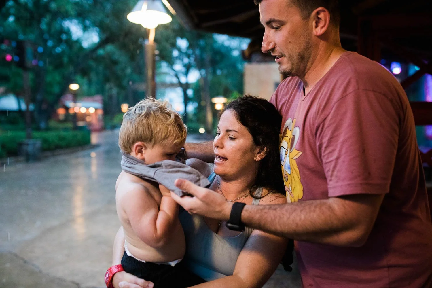 Parents help redress a toddler boy after playing in the rain.