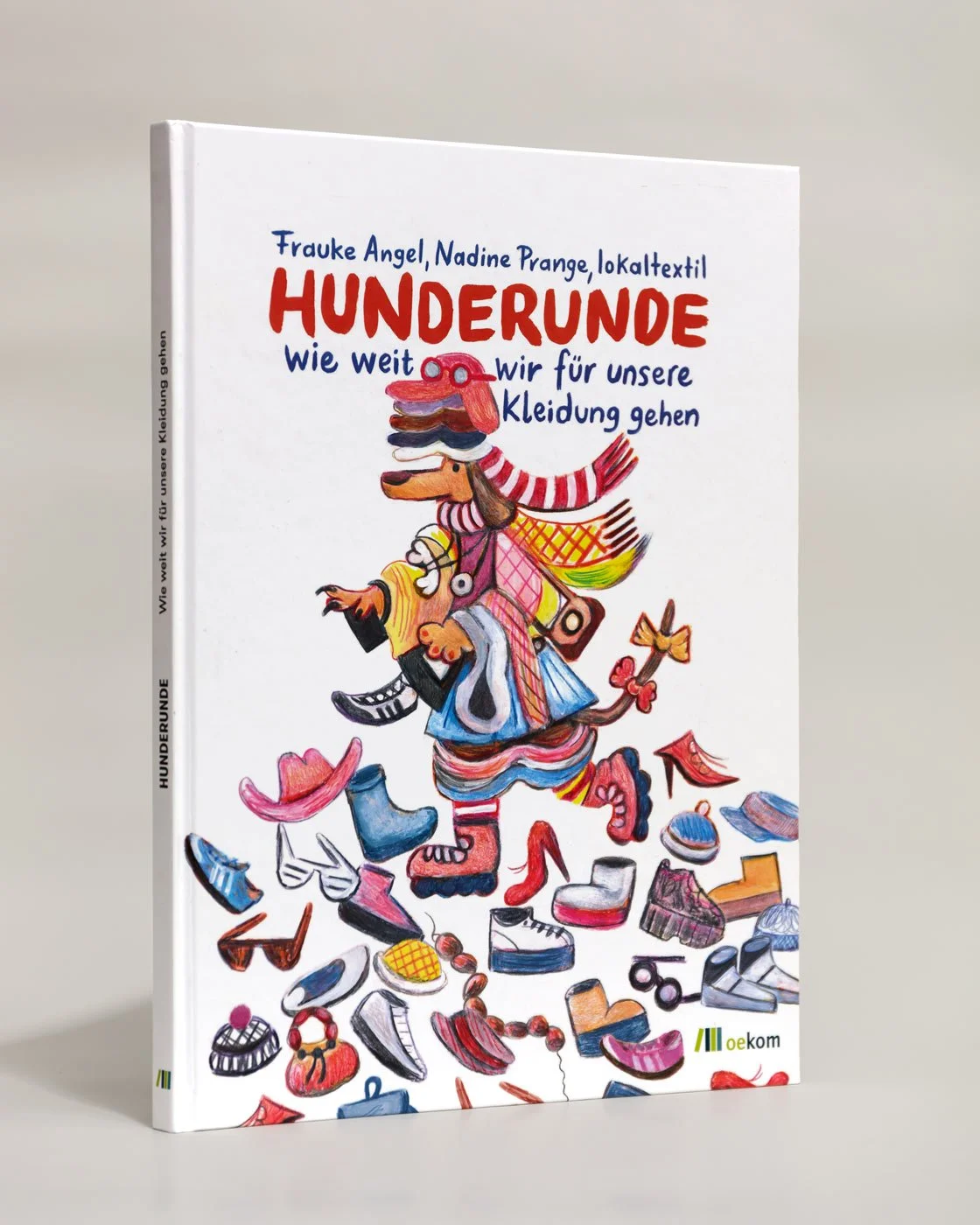 Die Vorderseite des Buchs Hunderunde wie weit wir für unsere Kleidung gehen. Abgebildet ist ein Hund, ein Dackel, der aufrecht auf einem Kleiderhaufen läuft. Der Hund trägt zu viel Kleidung.