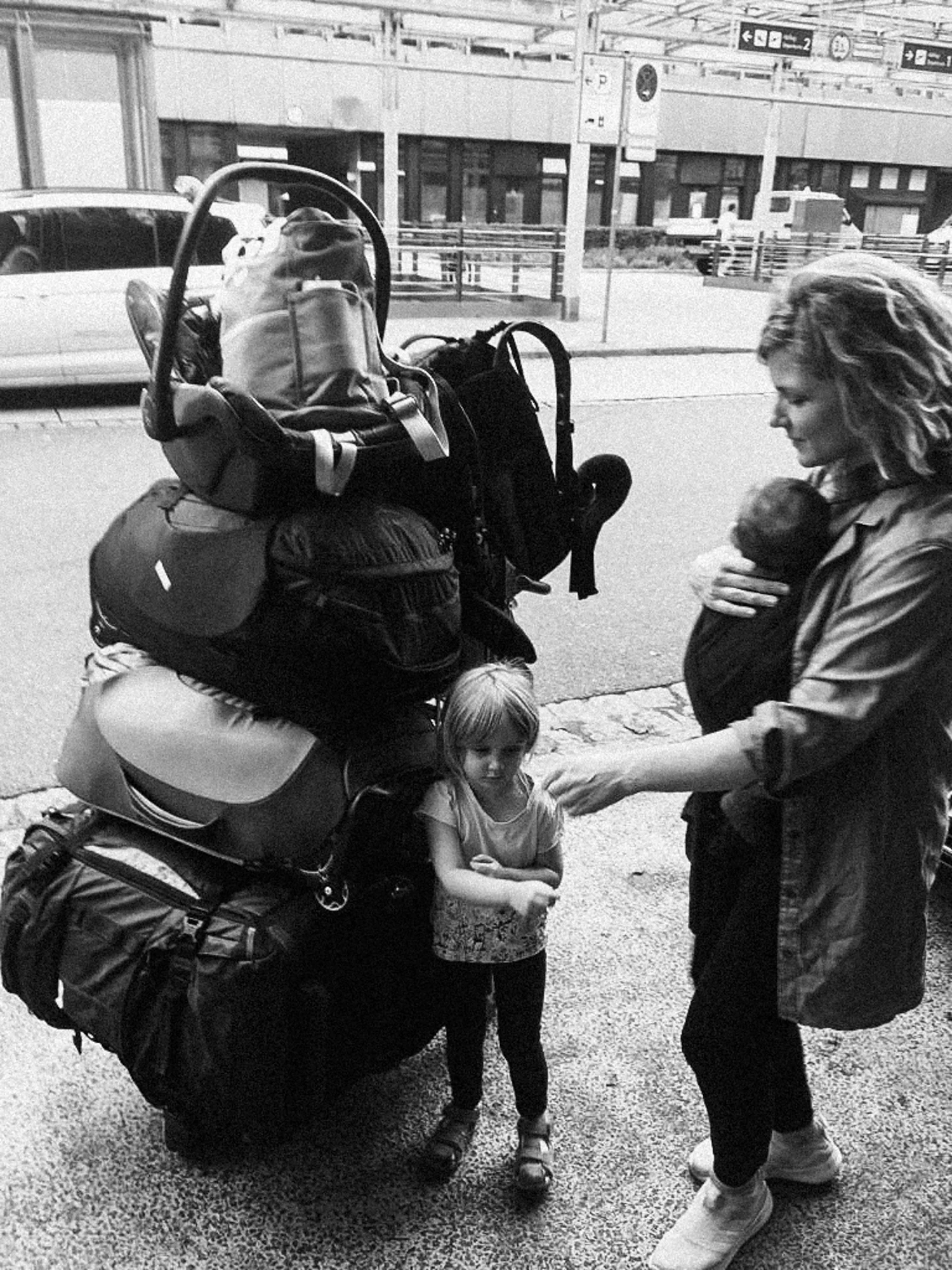 A woman, baby and daughter stand next to their tower of baggage at the airport.