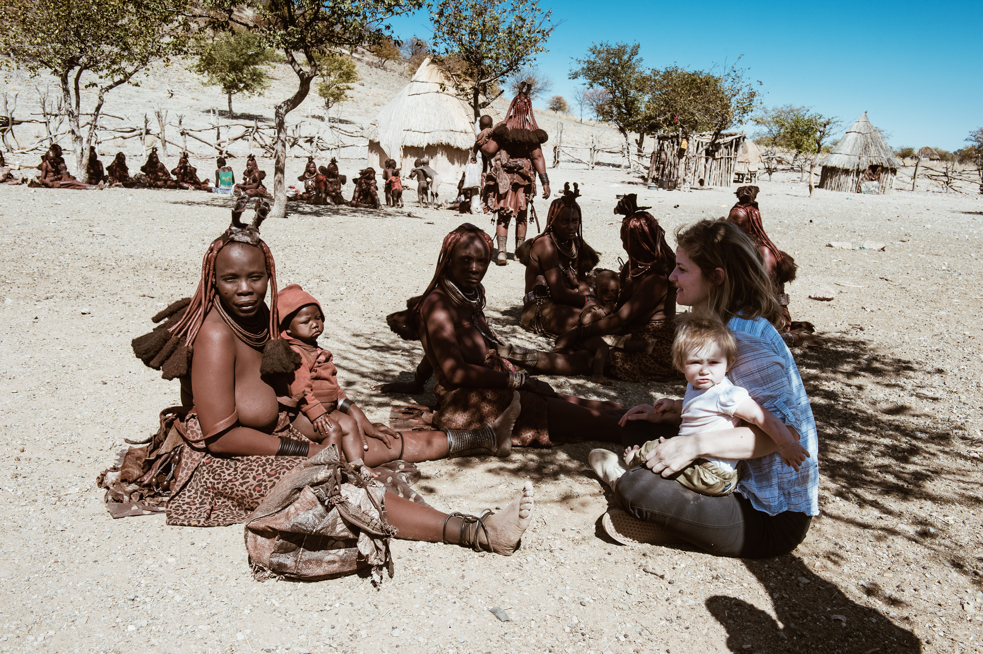 White tourist with a baby interacting with Himba women, Kaokoland, Namibia