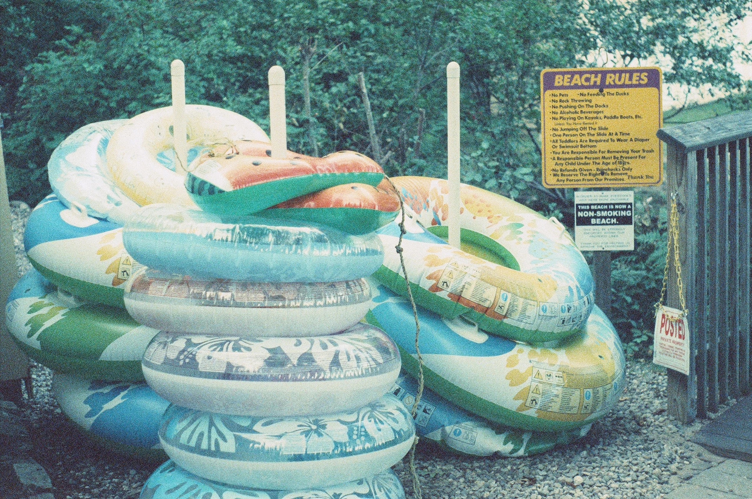 stacks of brightly colored floating tubes are piled up next to a sign that says "beach rules"