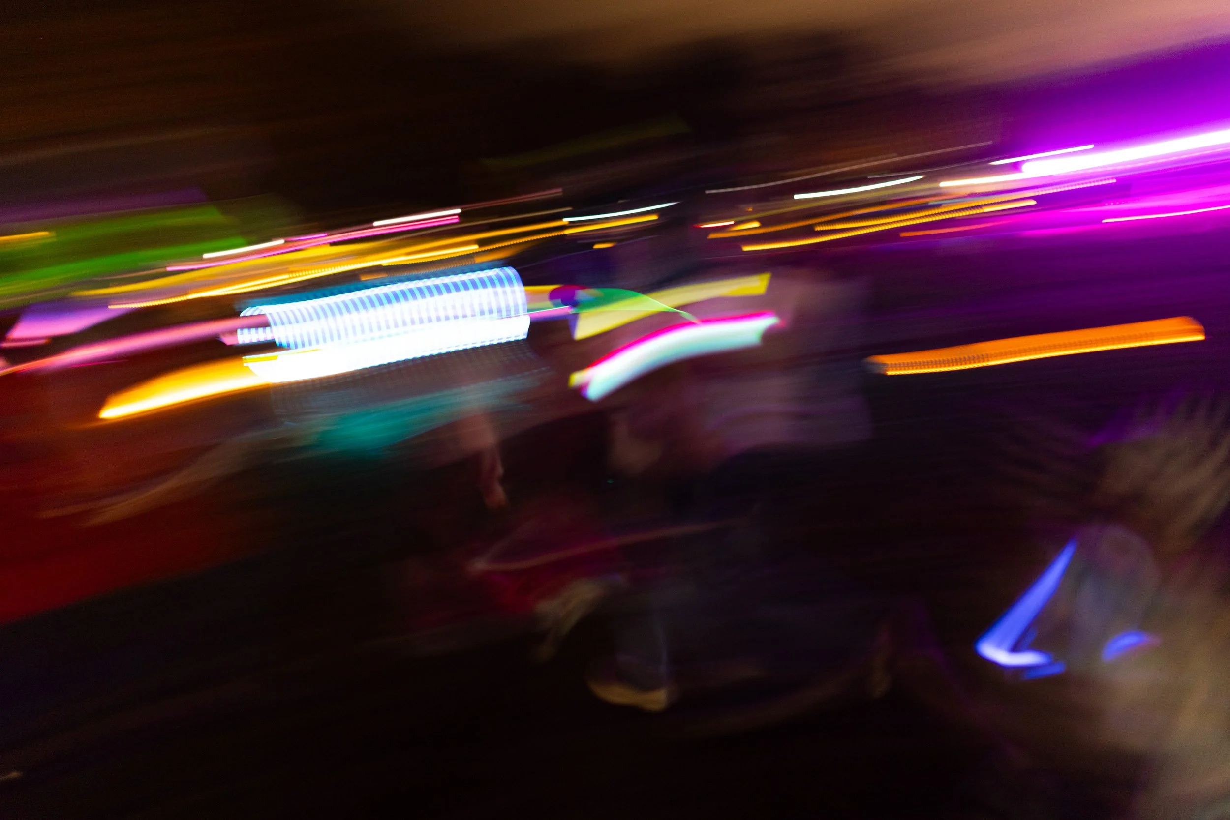 a motion capture, long exposure of people running holding glow sticks. the glowing lights create abstract lines through the photo in bright neon colors.