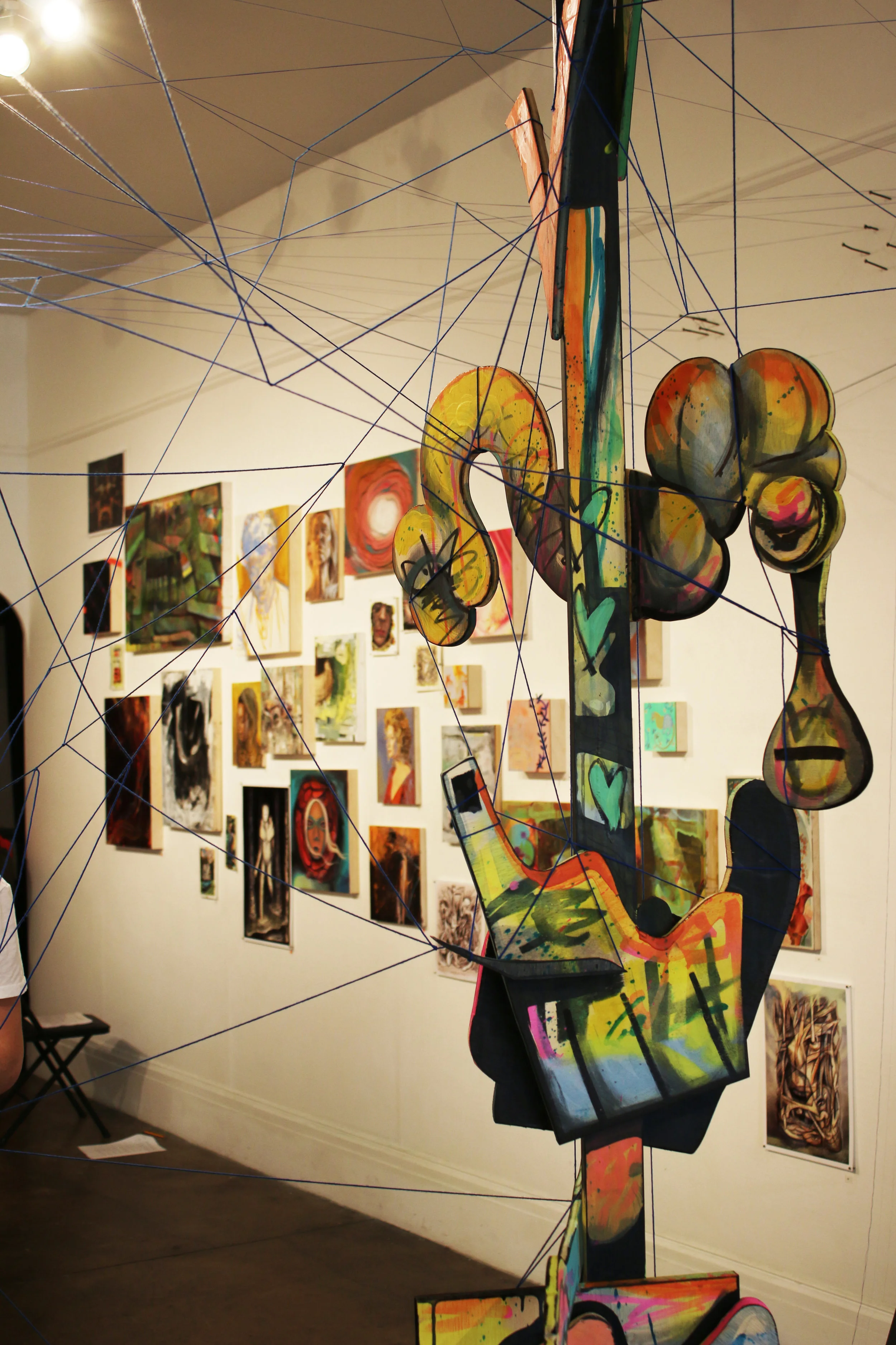 Sculpture by Zander Stefani in front of the salon-style wall of small works by both artists