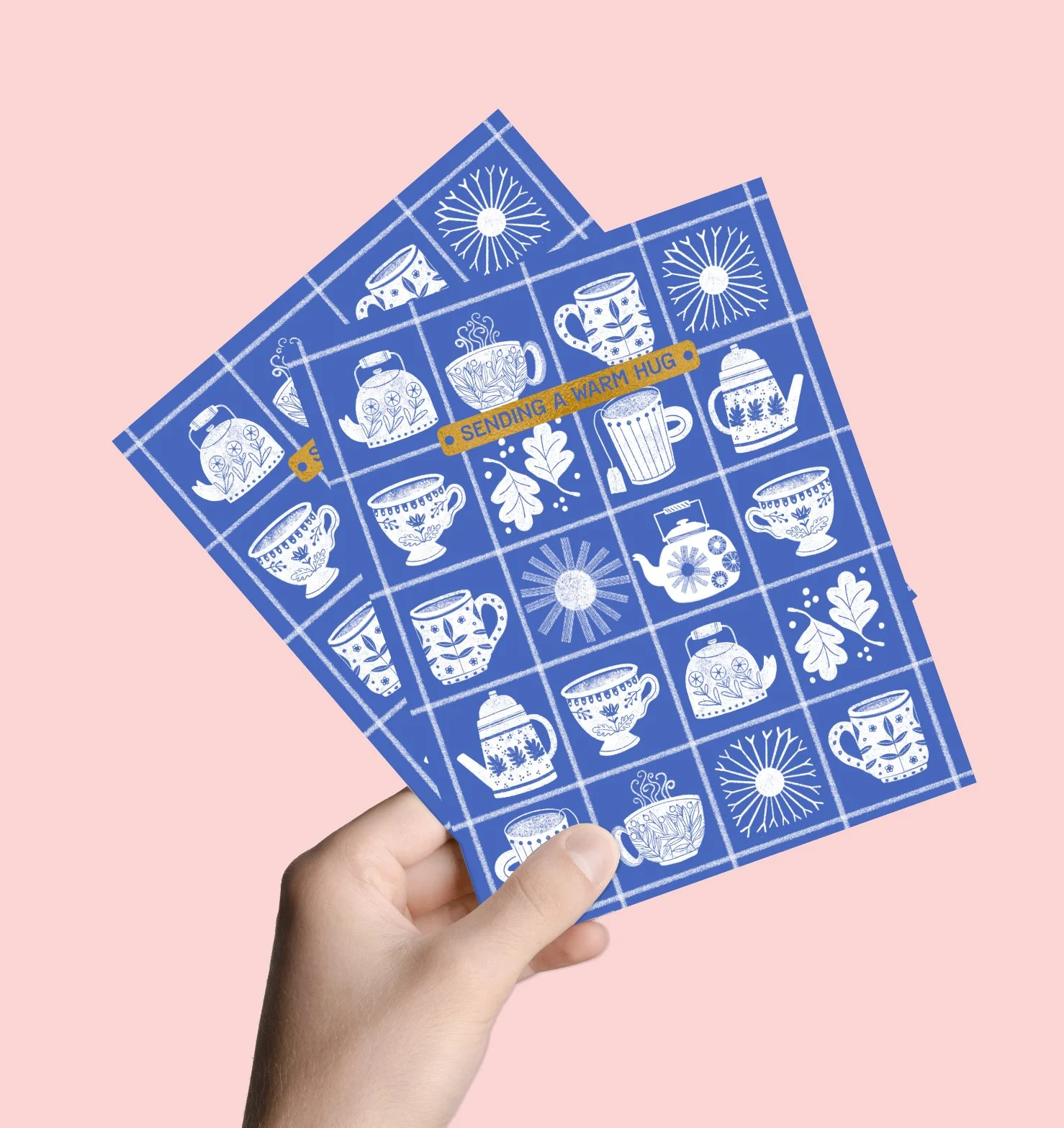 a hand holding 2 blue get well cards with teacup images on them against a soft pink background