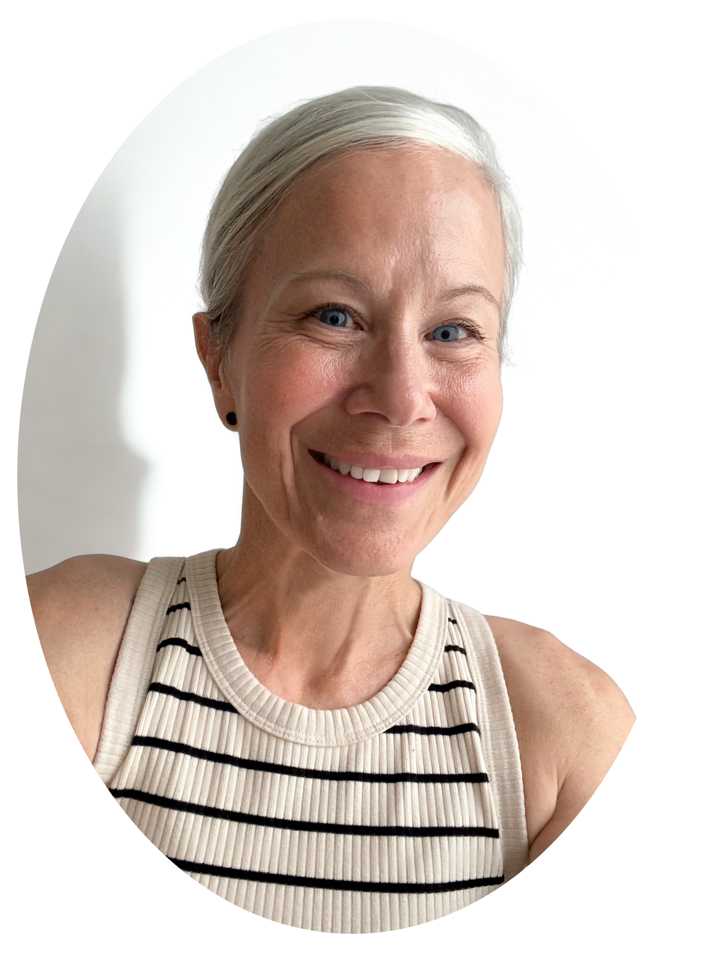 A smiling woman with short gray hair, blue eyes, and light skin wearing a sleeveless beige top with black stripes, standing against a white background.