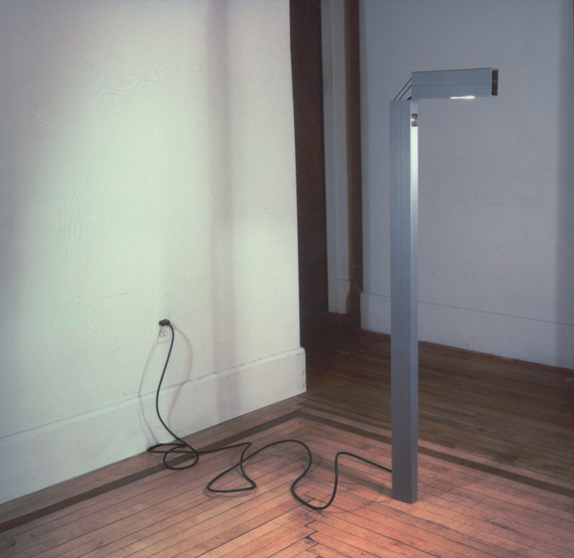  As minimal reaction to post-modern excess, a simple structural steel tube is used to create a floor lamp. The top of the lamp hinges, thus allowing for two directional lighting. In the standard position, the lamp produces ambient uplighting. In the 