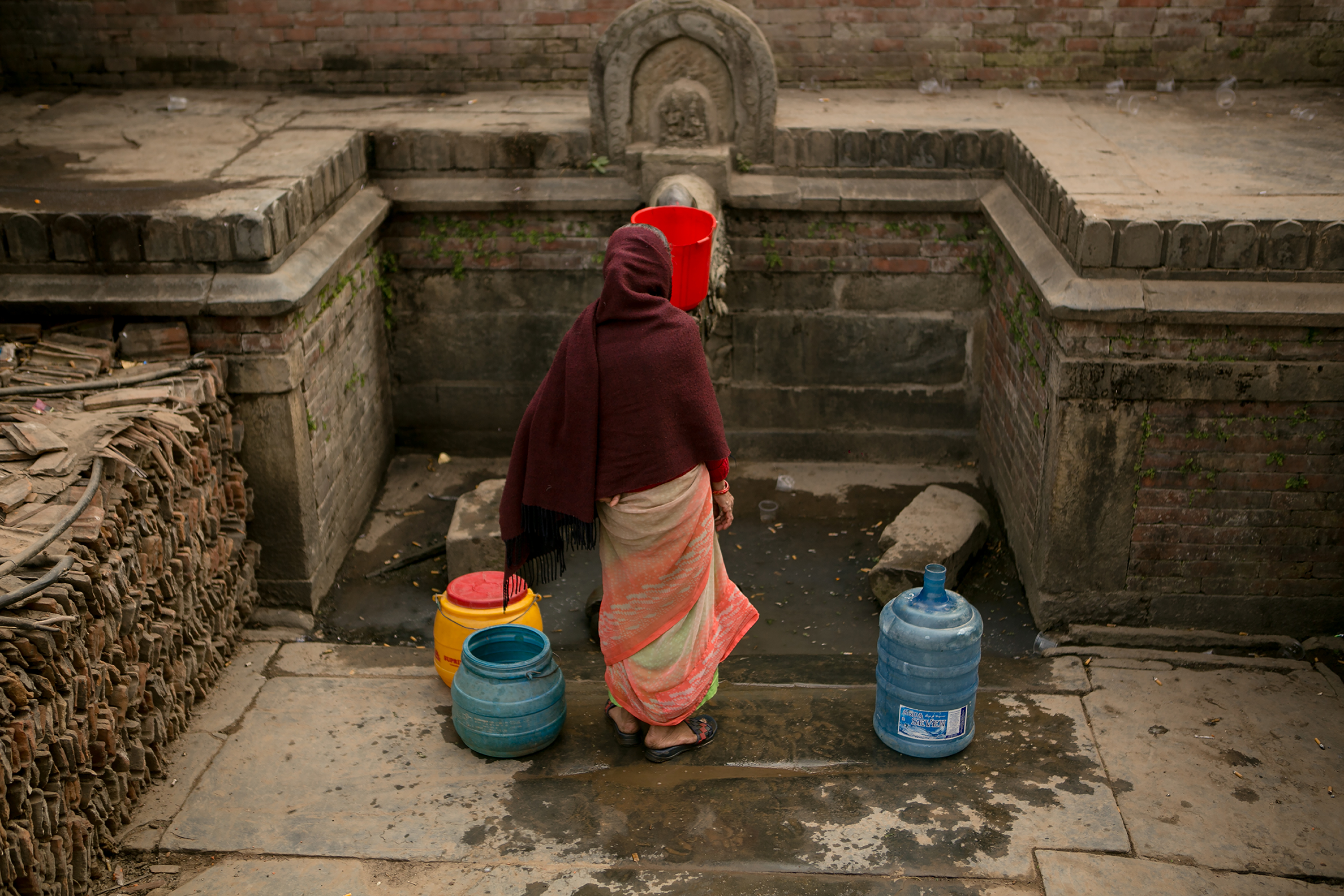 BHAKTAPUR, NEPAL — A woman stands still in front of a public well as she waits for water to fill her containers.