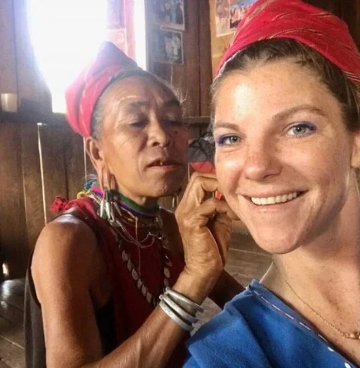 Two women wearing red head wraps, smiling for a selfie in a wooden room.