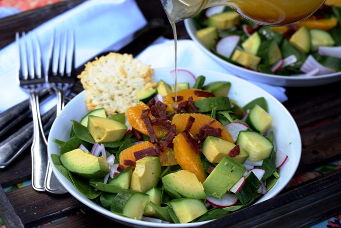 Spring Baby Spinach Salad being drizzled with Orange Vinaigrette served with a Parmesan Crisp