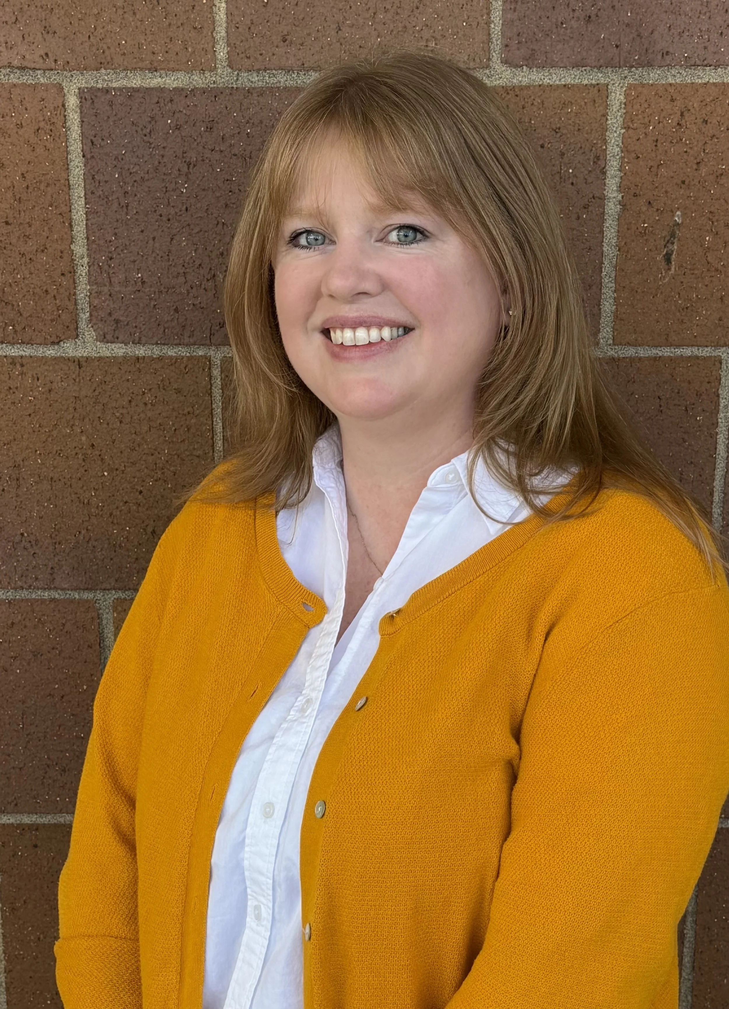 Program Administrator Laurel Fischer stands smiling in front of a brick wall