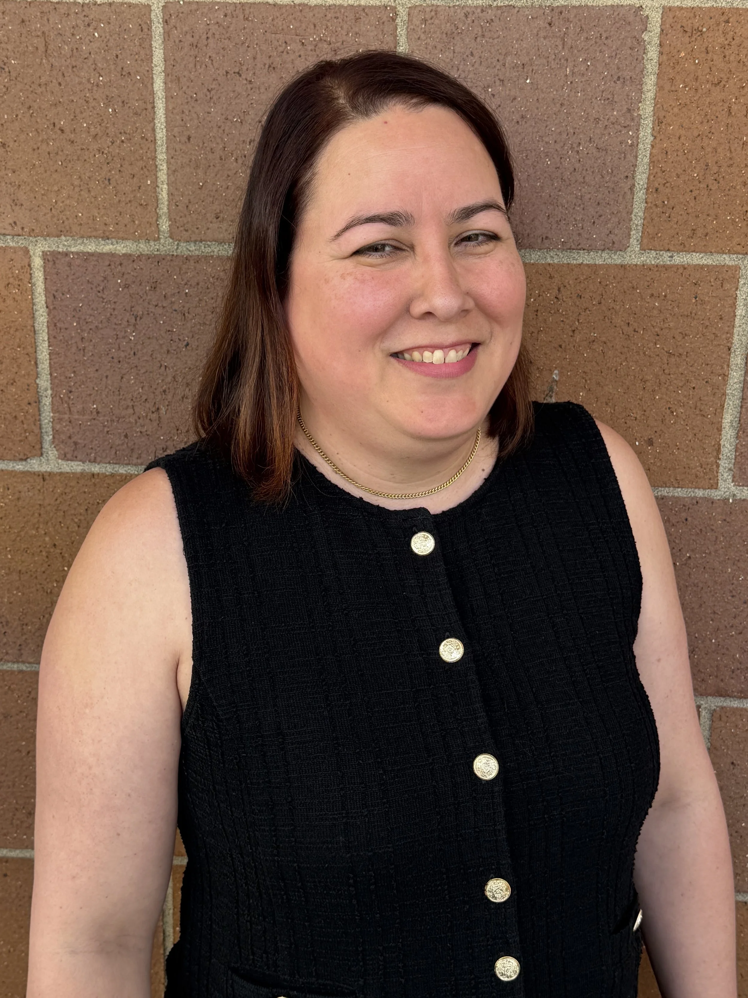 Dr. Jesabel Centeno stands smiling in front of a brick wall