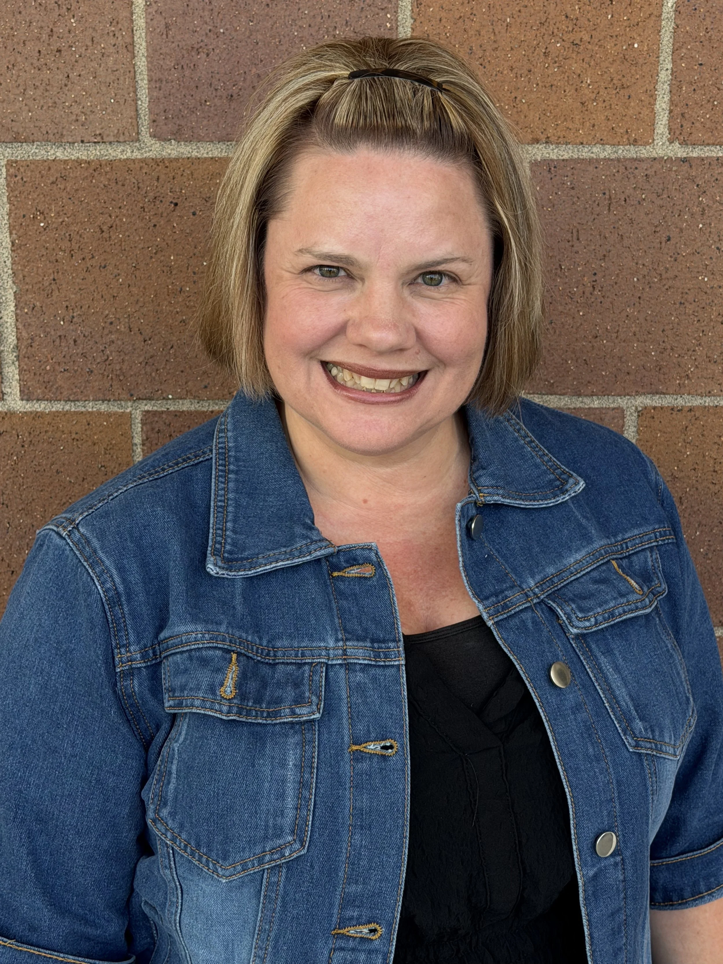 Sharyn Hoffert stands smiling in front of a brick wall