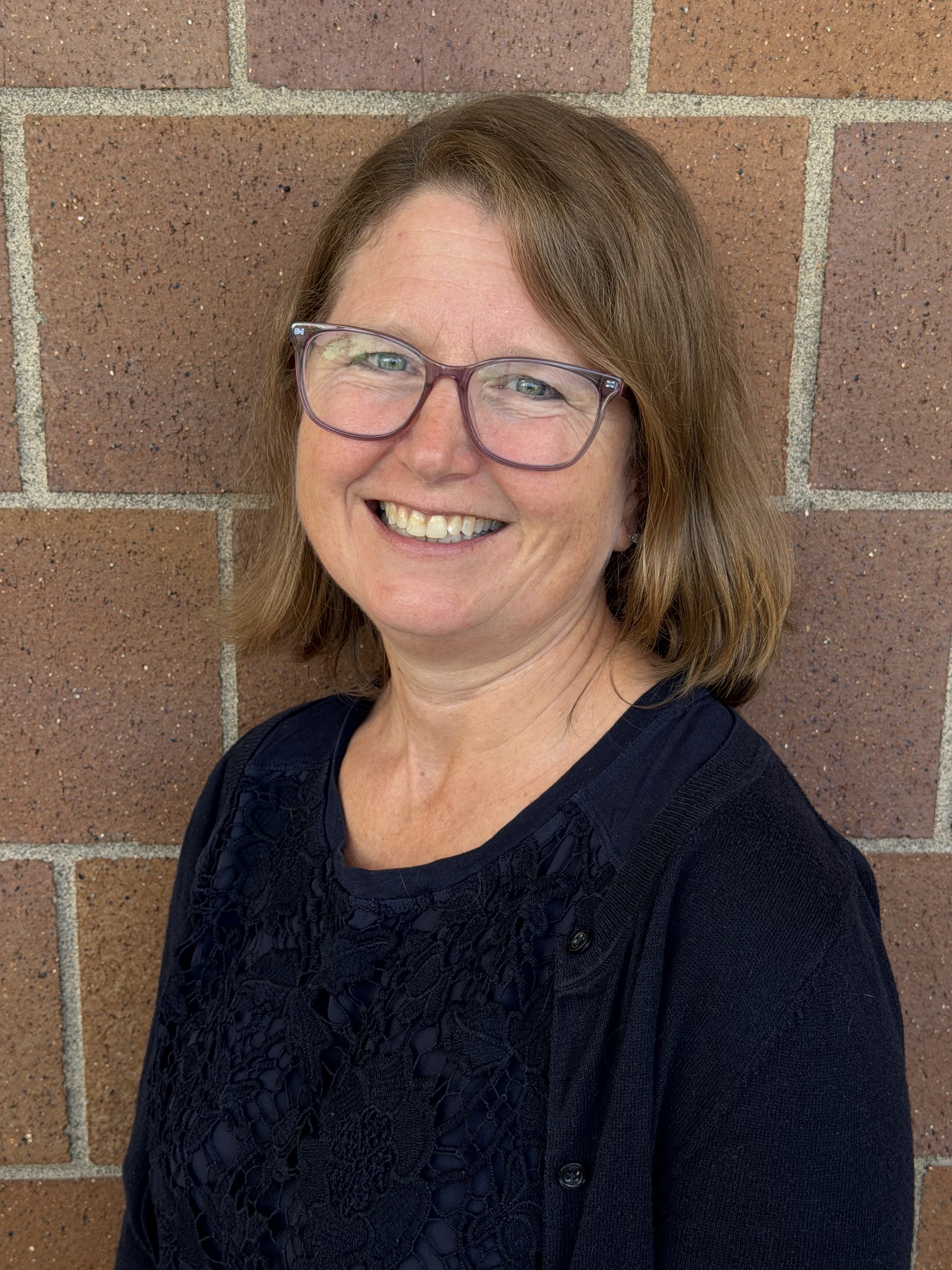 Beth Ferguson stands smiling in front of a brick wall