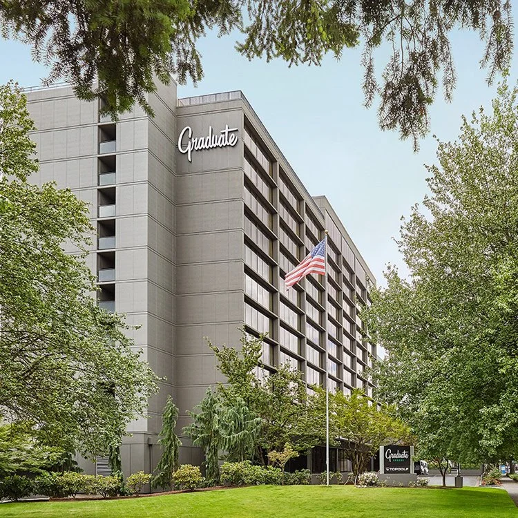 Exterior of the Graduate by Hilton Eugene hotel and conference center, including their front lawn and drive up. An American flag stands in the center of the field.