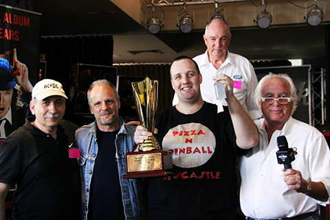 Pictured here winning the Australian AC/DC Pinball Championship (and holding the keys to a shiny new AC/DC pinball machine), with Gary Stern (Stern Pinball) and Mark Evans (AC/DC band member) at either side. Photo by the Australian Pinball League.